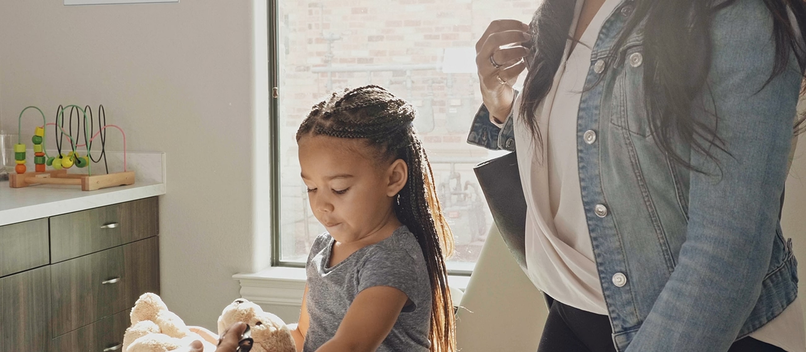 Child playing with teddy bear in bright room.