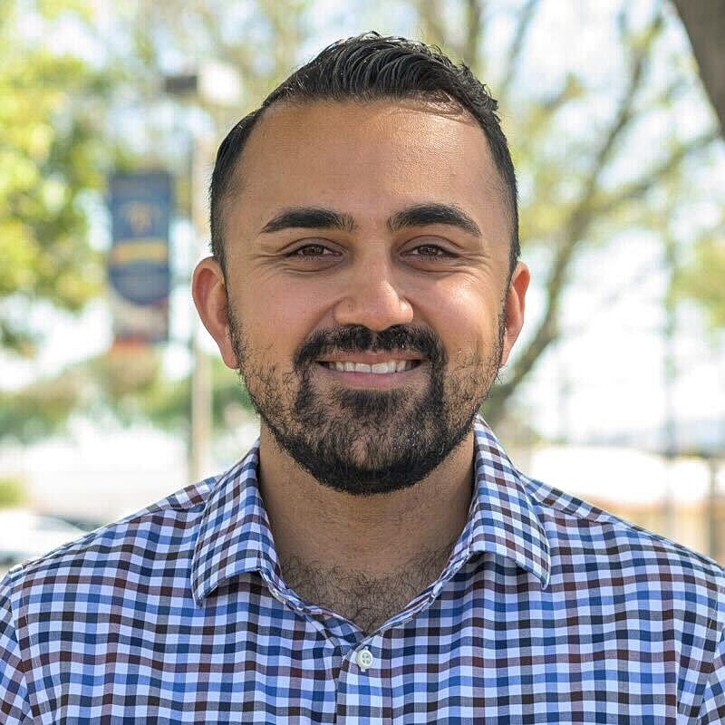 Smiling man in a checkered shirt outdoors.