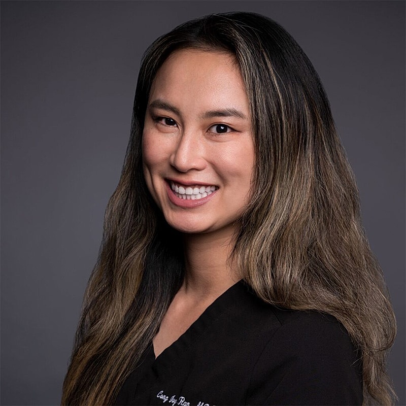 Smiling professional in medical attire against gray background.