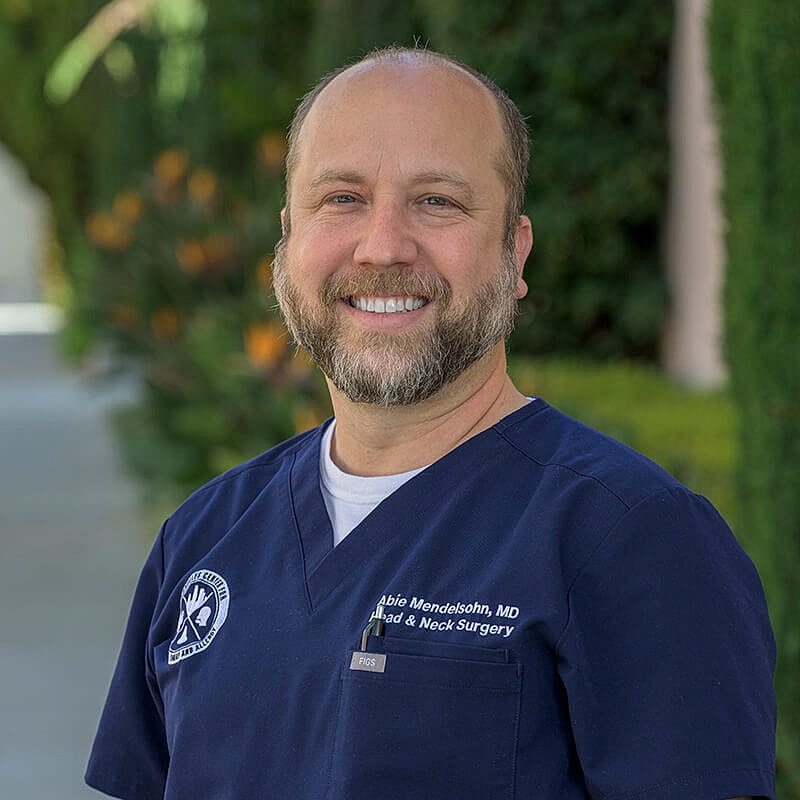 Smiling doctor in scrubs outdoors.
