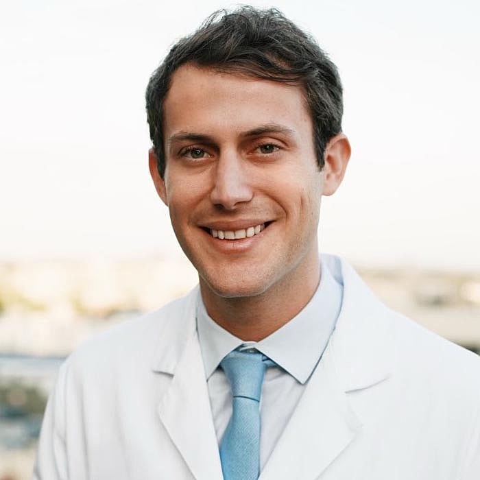 Smiling doctor in a white coat outdoors.