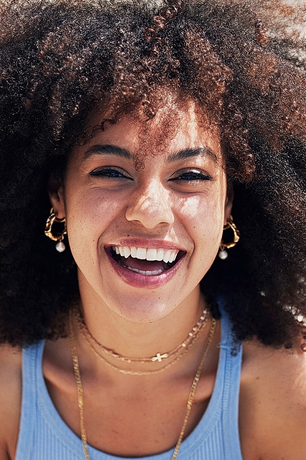 Smiling woman with curly hair and jewelry.