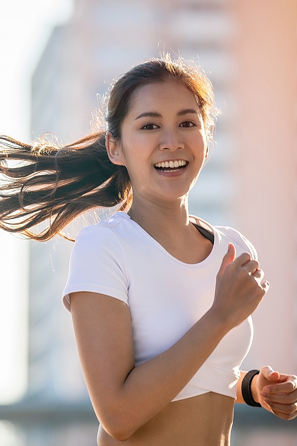 Smiling woman running outdoors in athletic wear.