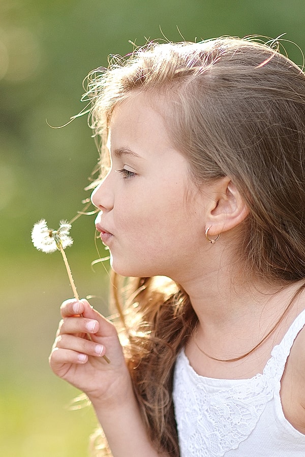 Girl blowing on dandelion seeds outdoors.