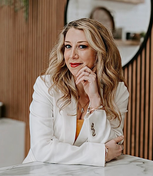 Smiling woman in white blazer, thoughtful pose.