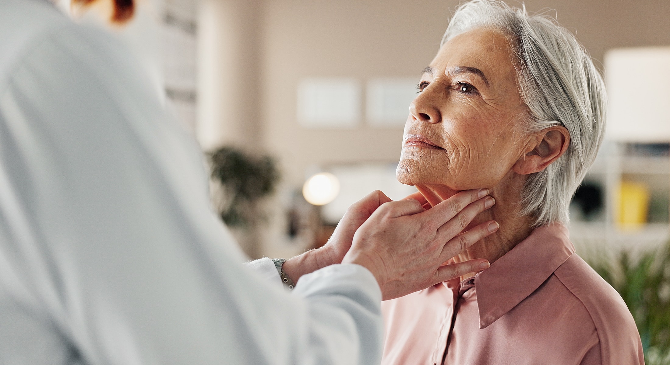 Doctor examining older woman's throat and neck.