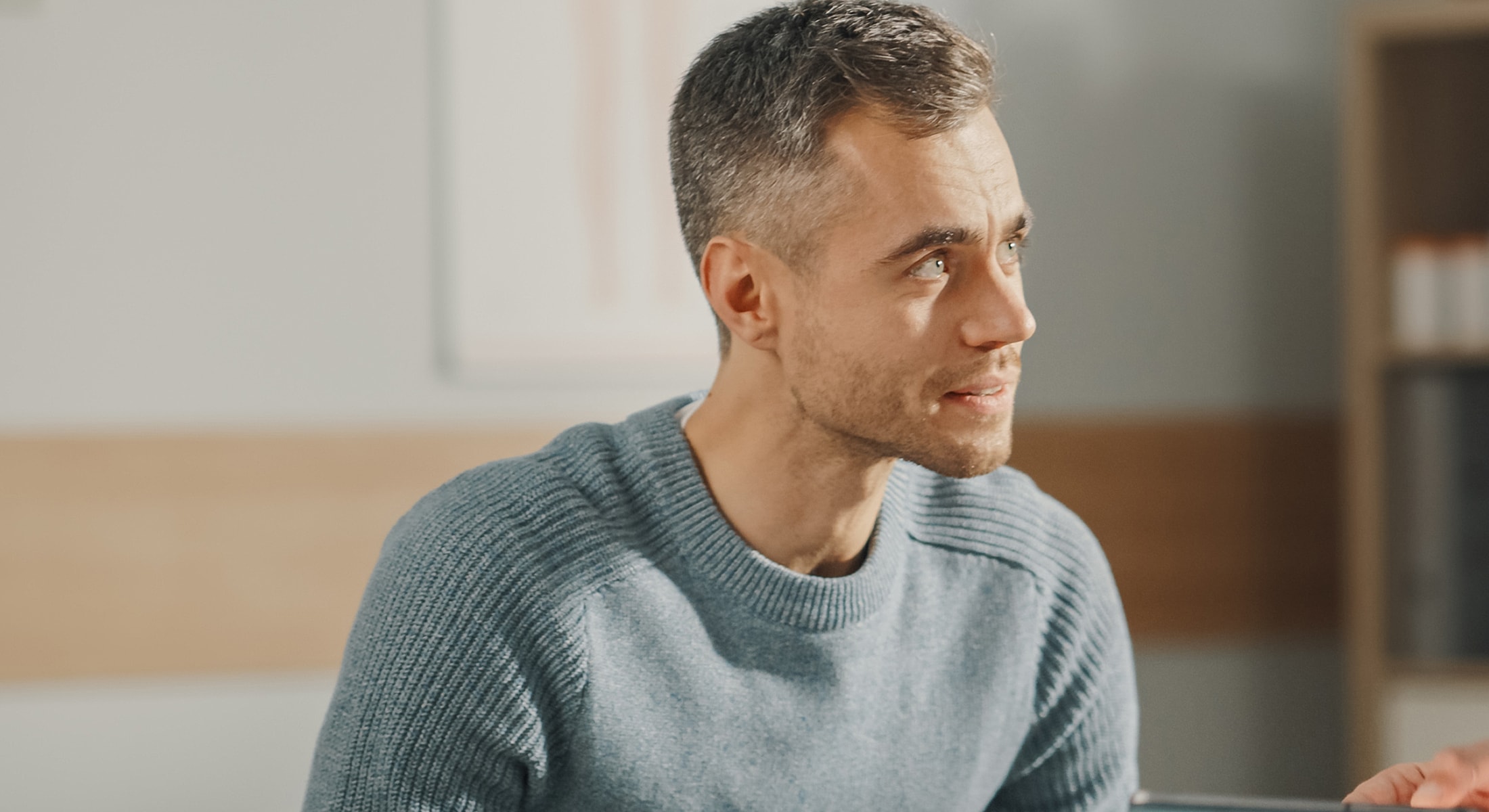 Man in blue sweater sitting and listening attentively.