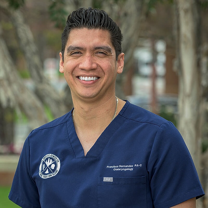 Male healthcare professional smiling outdoors in scrubs.