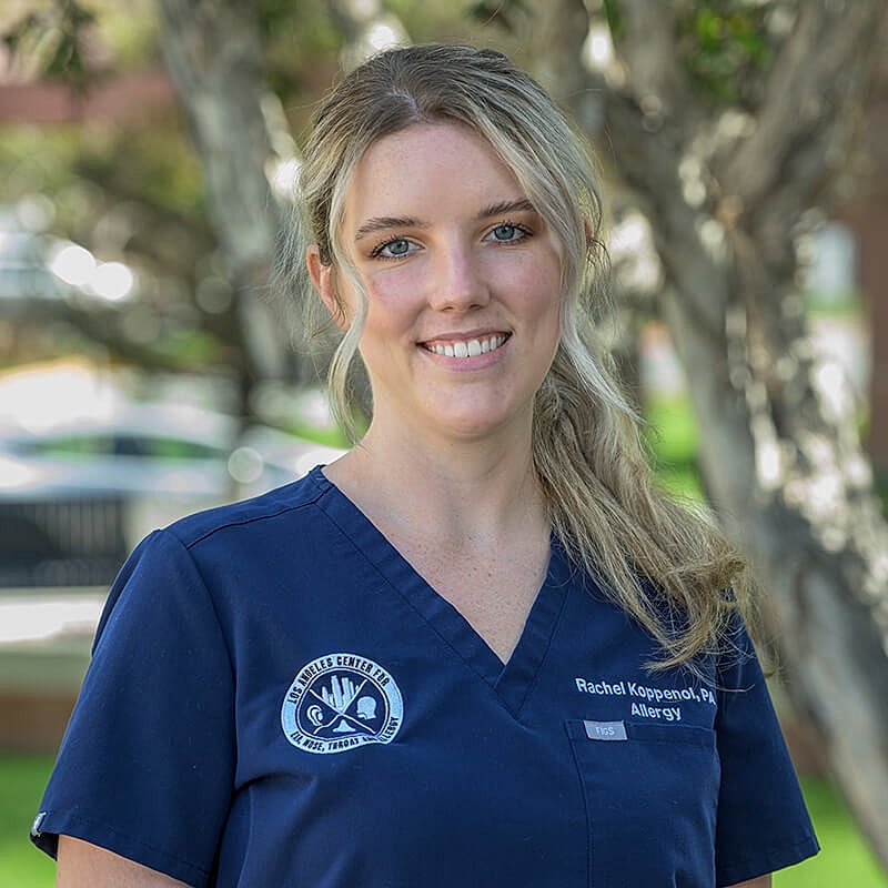 Health professional in scrubs smiling outdoors.