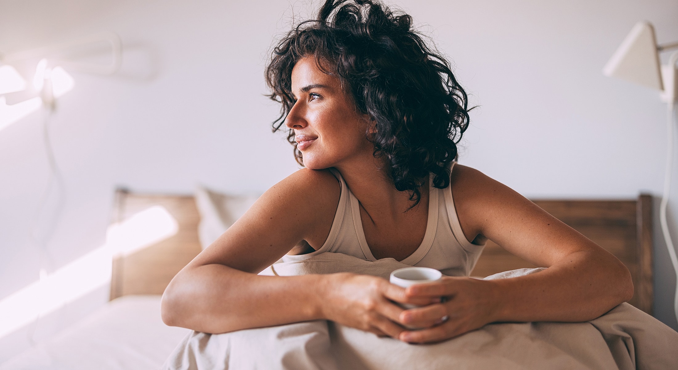 Woman holding a cup, looking thoughtfully outwards.
