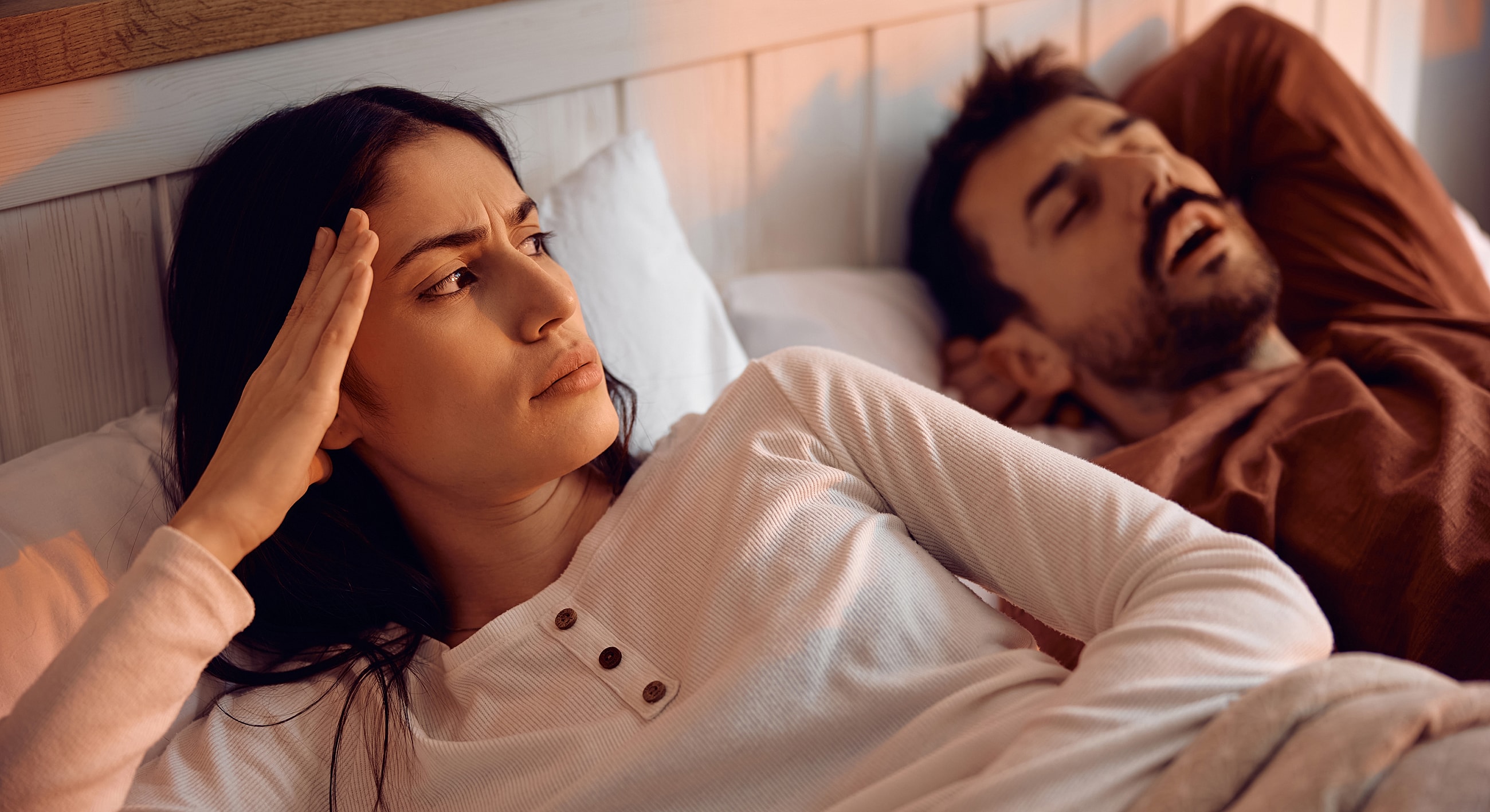 Frustrated woman with snoring partner in bed.