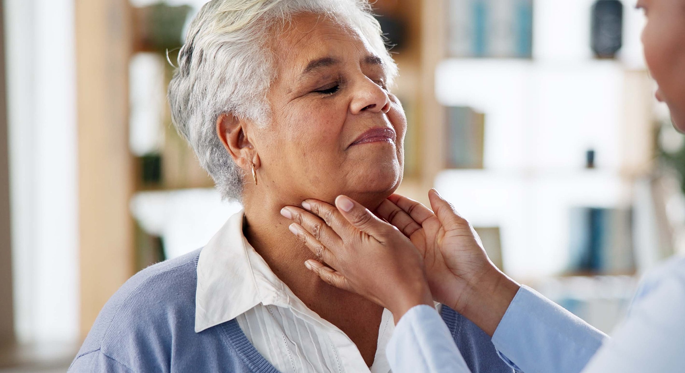 Healthcare professional examining senior woman's throat.