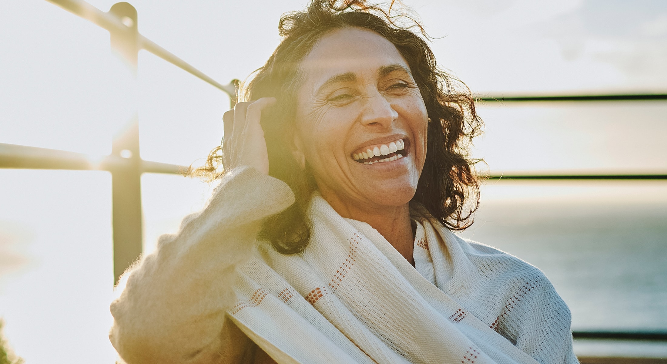 Woman smiling joyfully outdoors with sunlight.